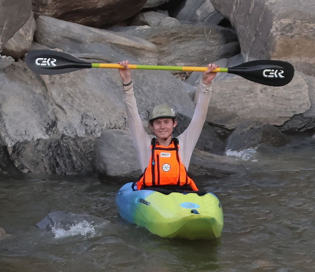 A kayaker holding a CEKR paddle overhead on the river.