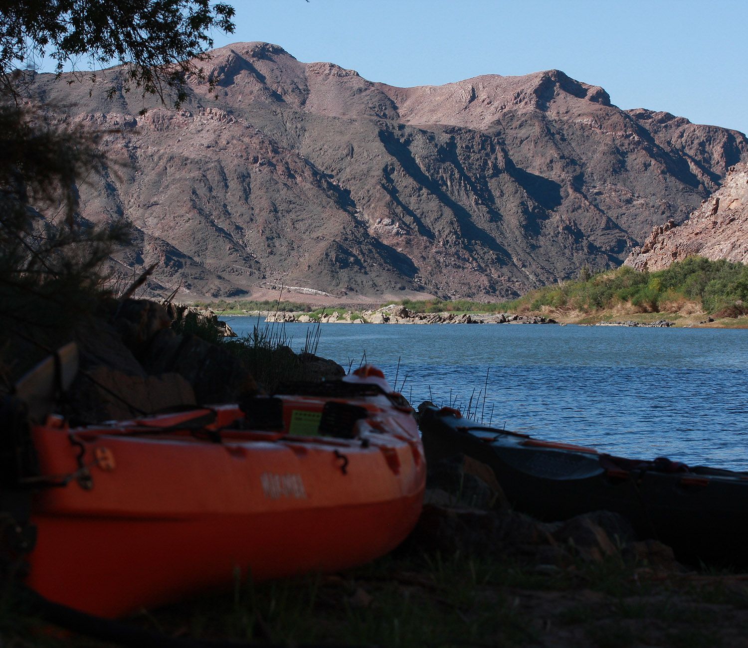 An orange expedition kayak on a rocky shoreline beside blue water.