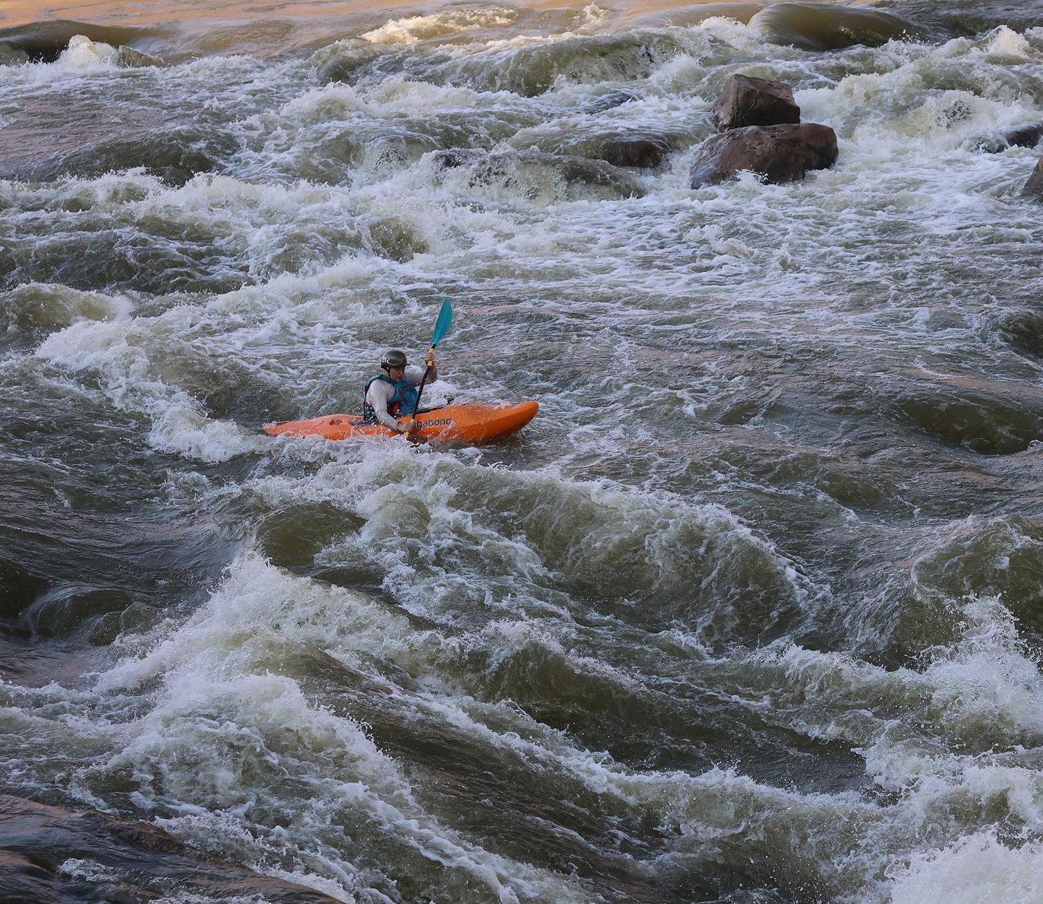 A kayaker in an orange boat running whitewater on the Orange River.